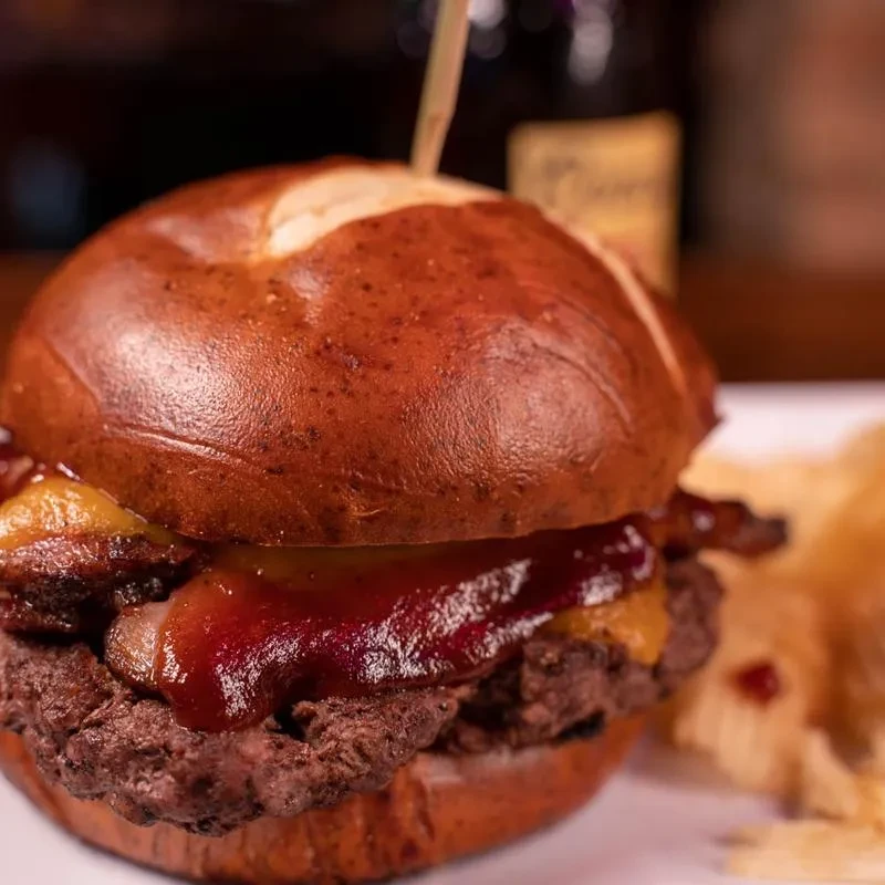 Burger on pretzel bun with bacon, cheese, and dark sauce.