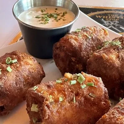 Plate of crispy, golden-brown fried food with herbs and dipping sauce.