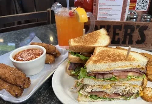 Close-up of a club sandwich meal with fried sides and an orange drink.