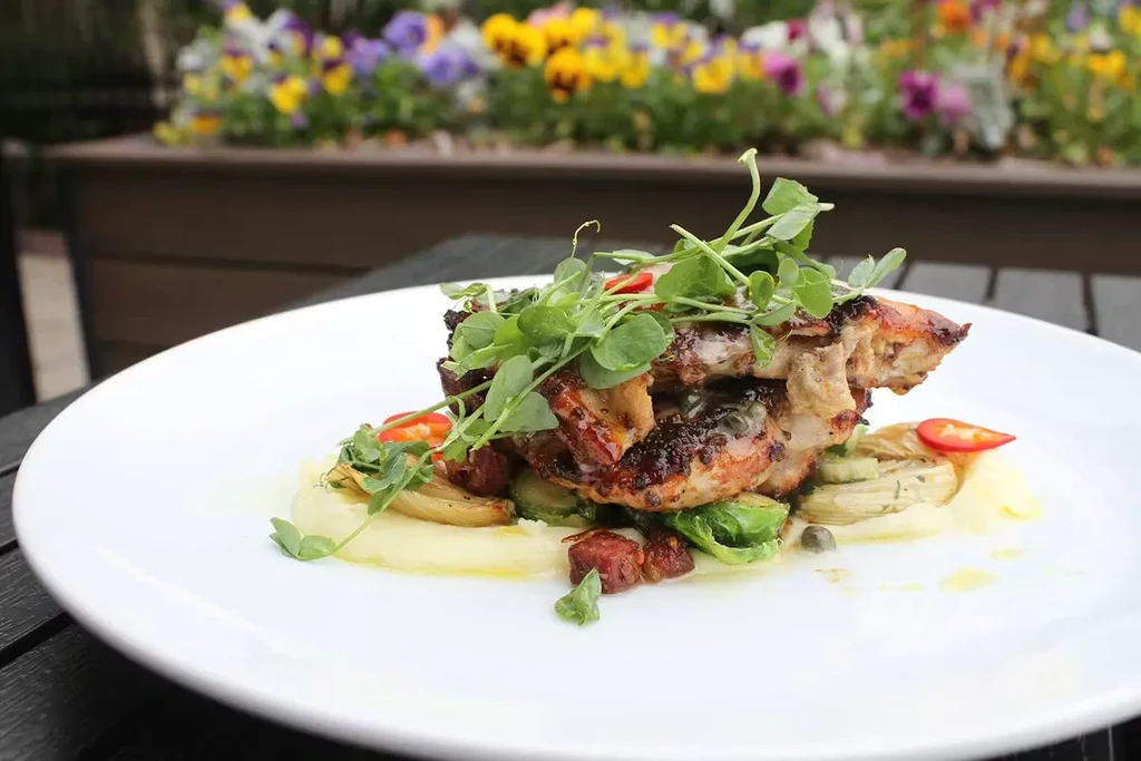 Plated roasted chicken, creamy purée, vegetables, and microgreens outdoors.