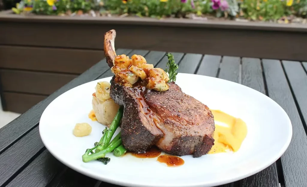 Gourmet bone-in meat chop, seafood, mashed potatoes, and broccolini.