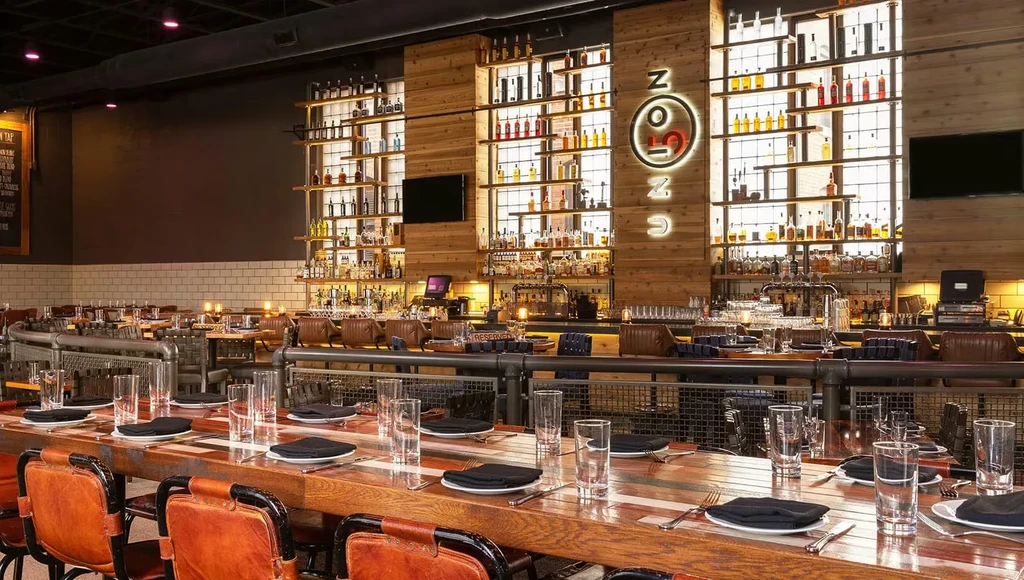 Empty modern industrial restaurant with rustic tables and a prominent lit bar.