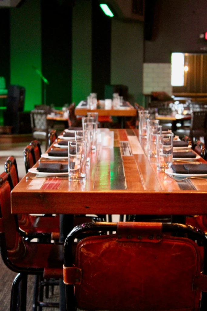 Empty, dim restaurant with set communal wooden table and leather chairs.