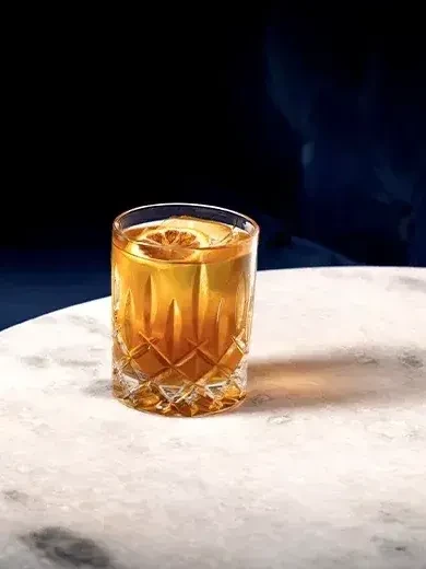 Amber drink with citrus slice in a faceted cut-glass tumbler.