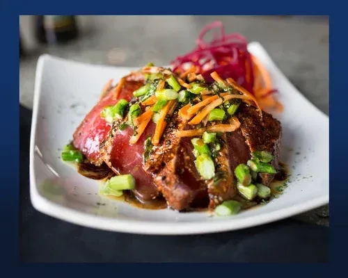 Seared tuna with green onions, carrots, and dark sauce on white plate.