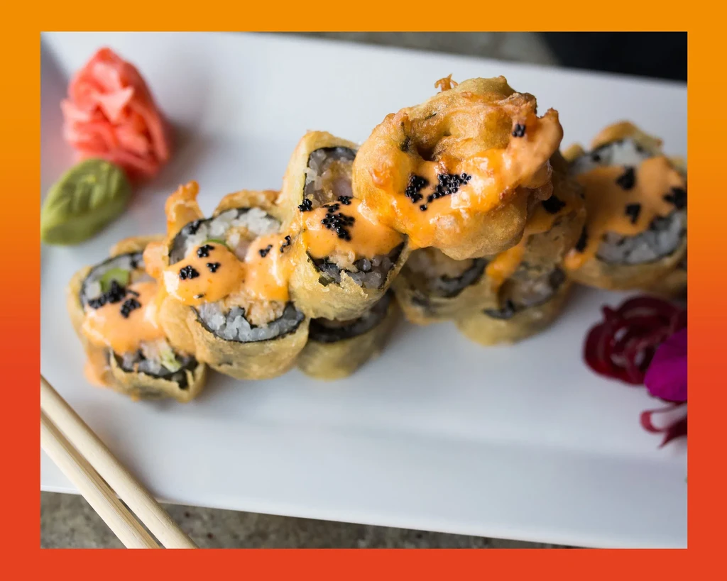 Plated deep-fried sushi rolls with orange sauce, roe, ginger, and wasabi.