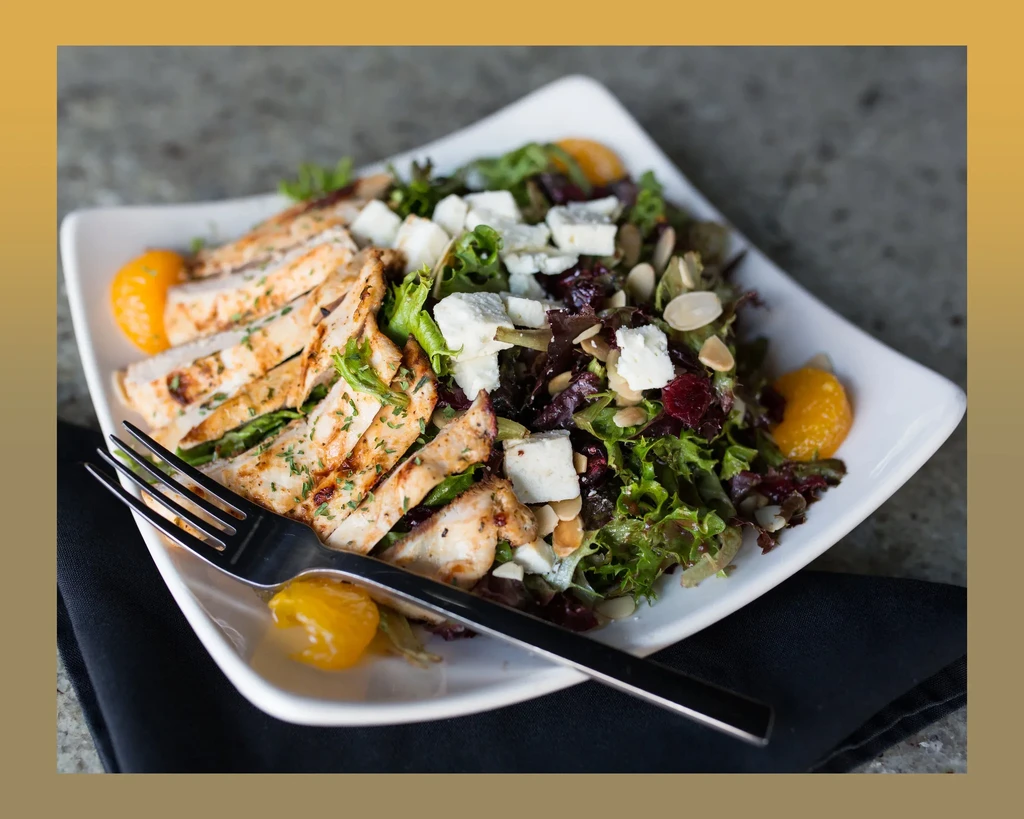 Plated grilled chicken salad with mixed greens, feta, and orange slices.