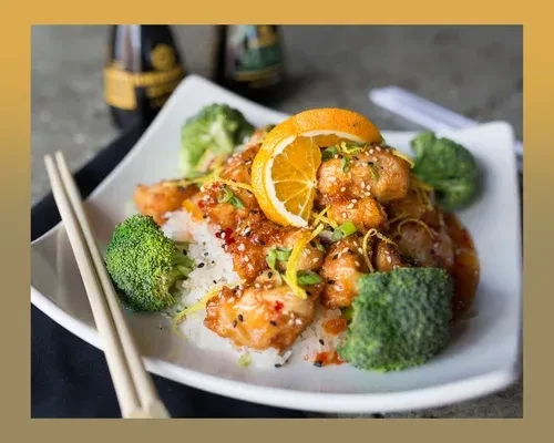 Orange chicken with rice, broccoli, sesame, green onions, and chopsticks.
