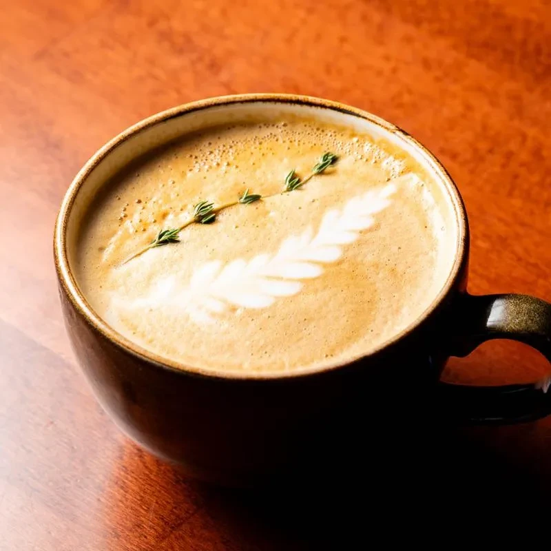 Close-up of a latte with leaf art, thyme sprig, on wood.