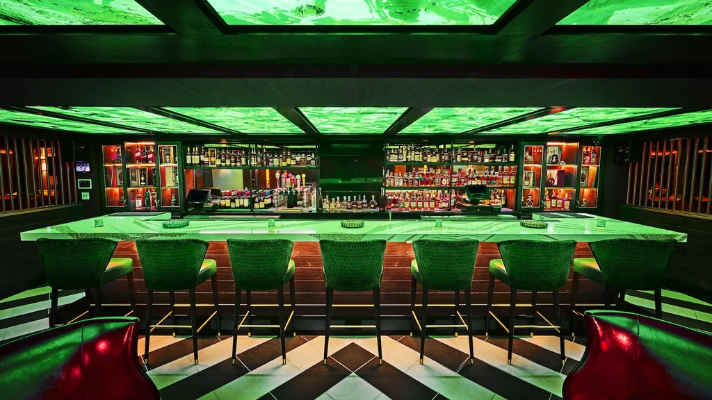 Modern bar interior with neon green glow, chevron floor, and empty stools.