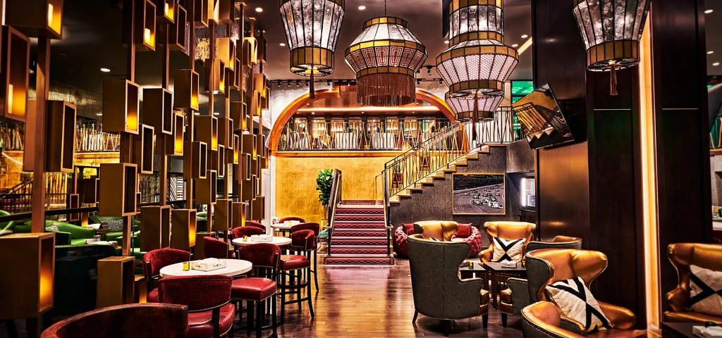 Grand red-carpeted staircase, ornate chandeliers, and plush seating.