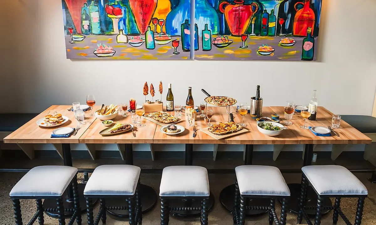 Long wood table set with pizzas, shared plates and wine bottles