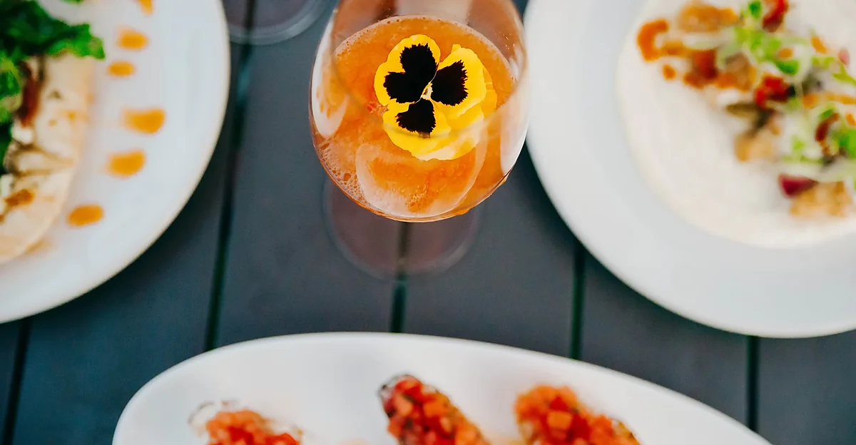 Overhead view of a cocktail with edible flower beside plated dishes