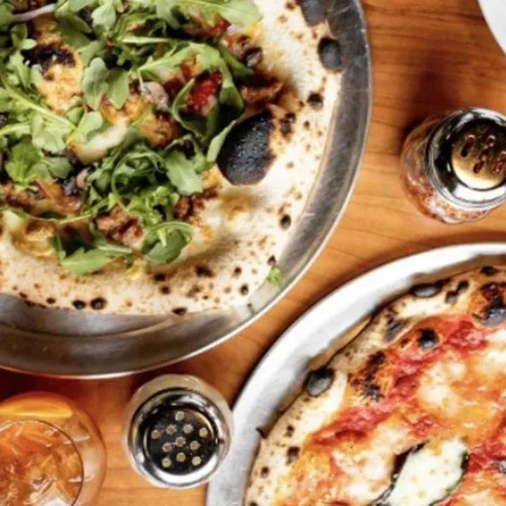 Two pizzas, one with arugula, one with zucchini, on a wooden table.