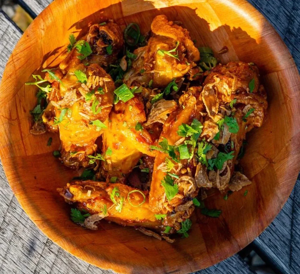 Cooked chicken in savory sauce, garnished with herbs in a wood bowl.