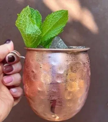 Hammered copper mug with mint and ice held by a hand.