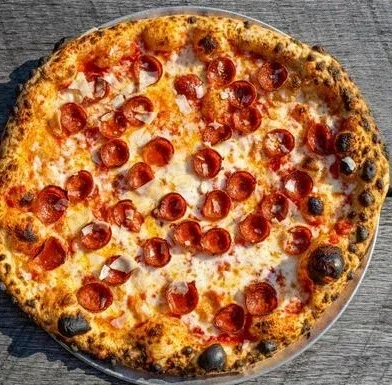 Round pepperoni pizza on a pan, overhead on a wooden surface.