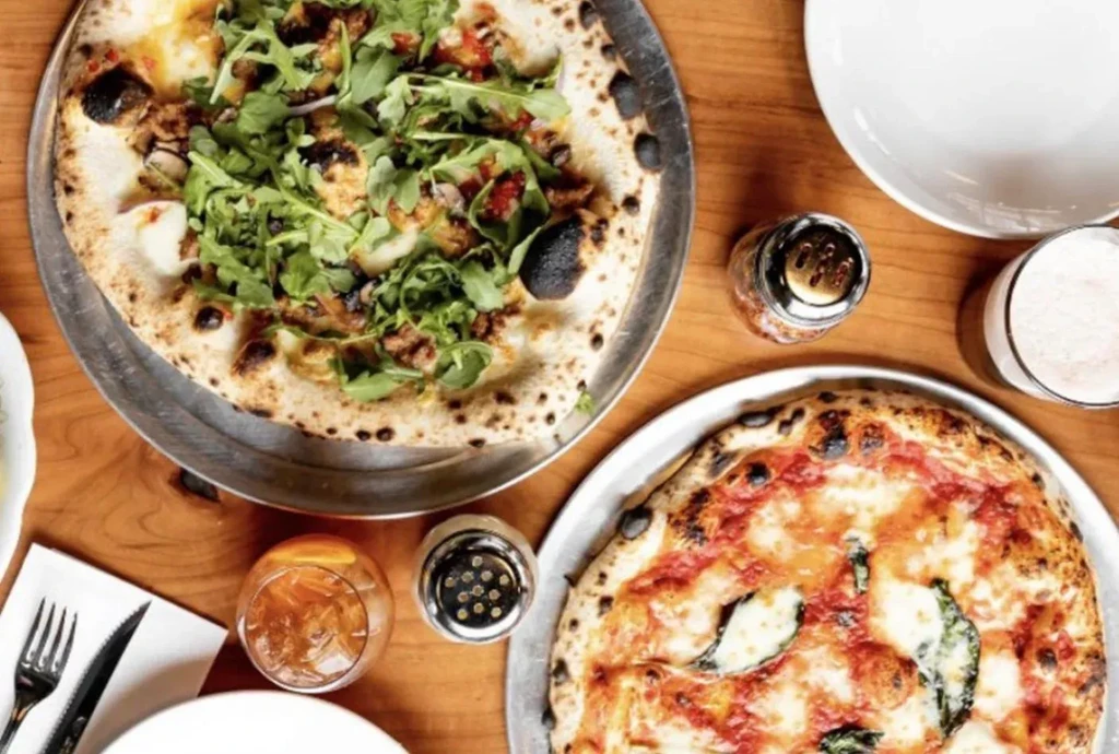Overhead of two distinct Neapolitan pizzas on a rustic wooden table.
