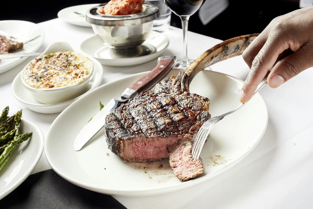 Medium-rare tomahawk ribeye steak with sides in an upscale restaurant.