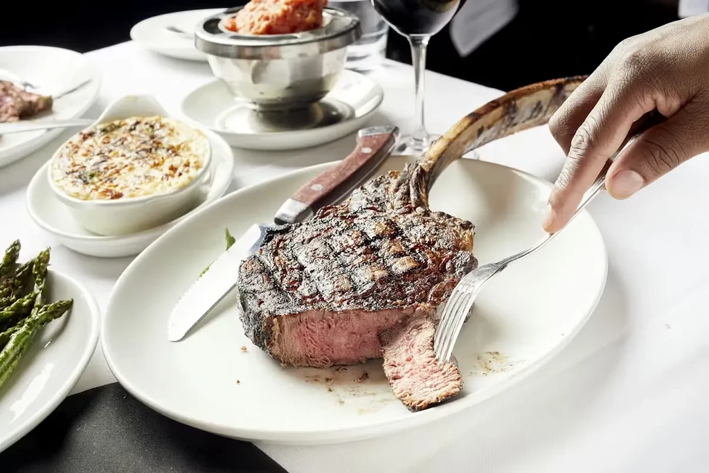 A seared tomahawk steak, medium-rare, with a slice cut by a fork.