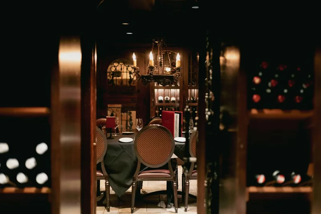 Elegant restaurant dining room with set table, chandelier, and wine racks.