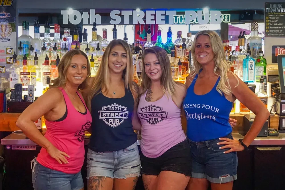 Four smiling 10th Street Pub staff behind a well-stocked bar.