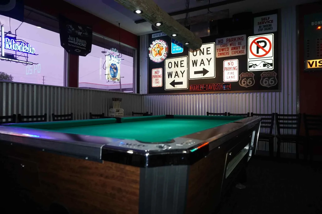 Green felt pool table inside a dim bar with road sign decor.