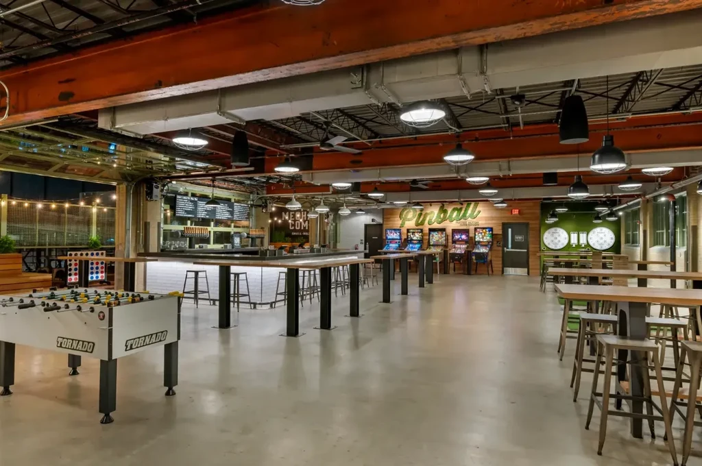 Industrial entertainment venue with bar, pinball machines, darts, and foosball.