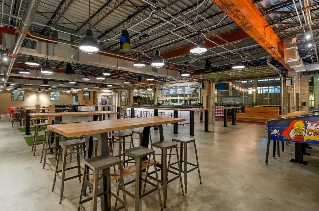 Empty modern industrial restaurant with communal tables, games, and outdoor patio.