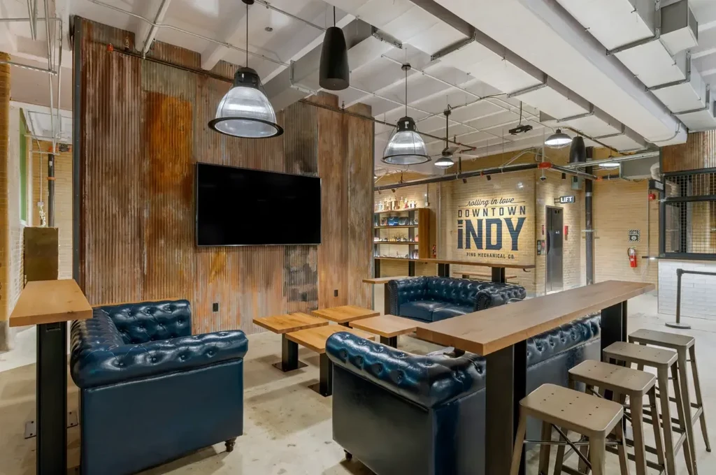 Industrial-chic lounge interior featuring sofas, high-top bar, and "PING MECHANICAL CO." sign.