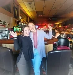 Two smiling women wave in a bar with an Old Key Tavern sign.