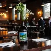 Dark UPLAND growler vase with flowers on a dim restaurant table.