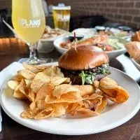 Close-up of a burger with greens, potato chips, and Upland beer.