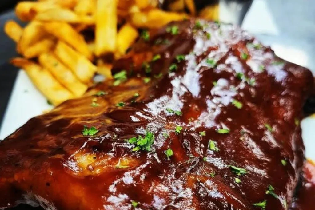 A rack of BBQ ribs with glossy sauce, herbs, and french fries.