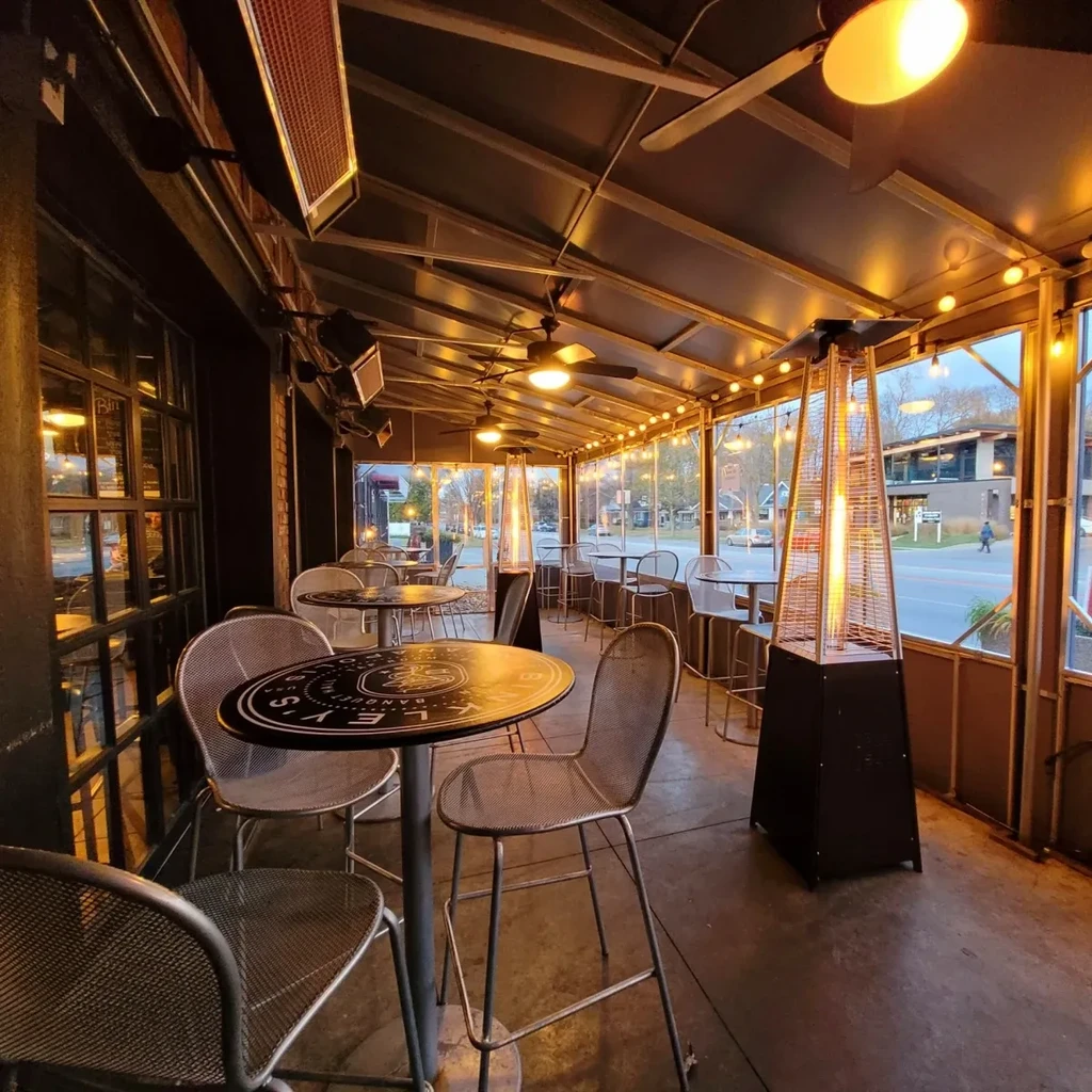 Enclosed restaurant patio with tables, heaters, string lights, and street view.