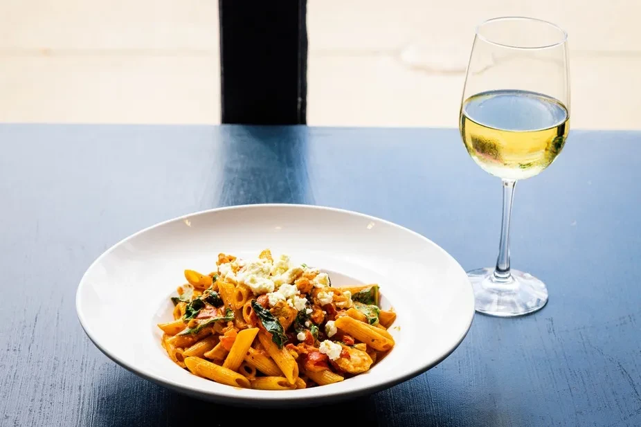 Penne pasta with red sauce, greens, crumbled cheese, and white wine.