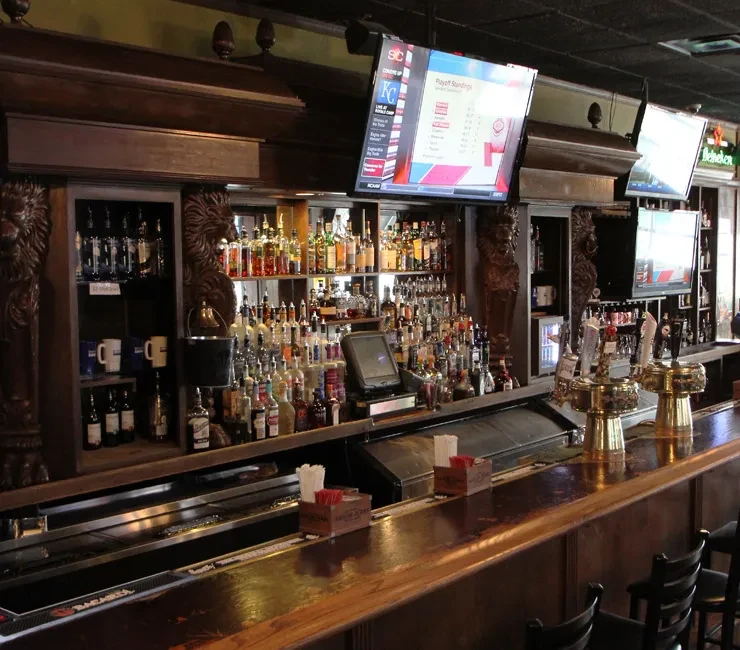 Dark wooden bar counter with liquor bottles and TVs showing standings.