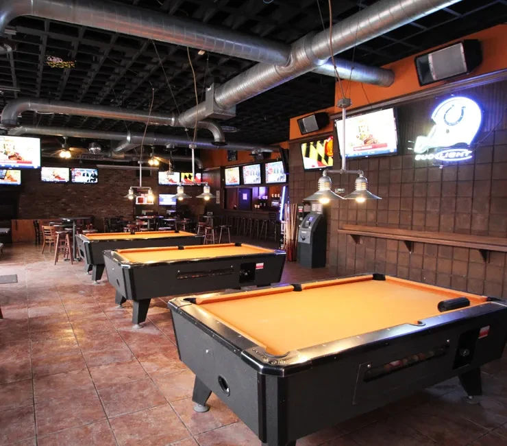Three orange pool tables in an empty industrial-style sports bar.