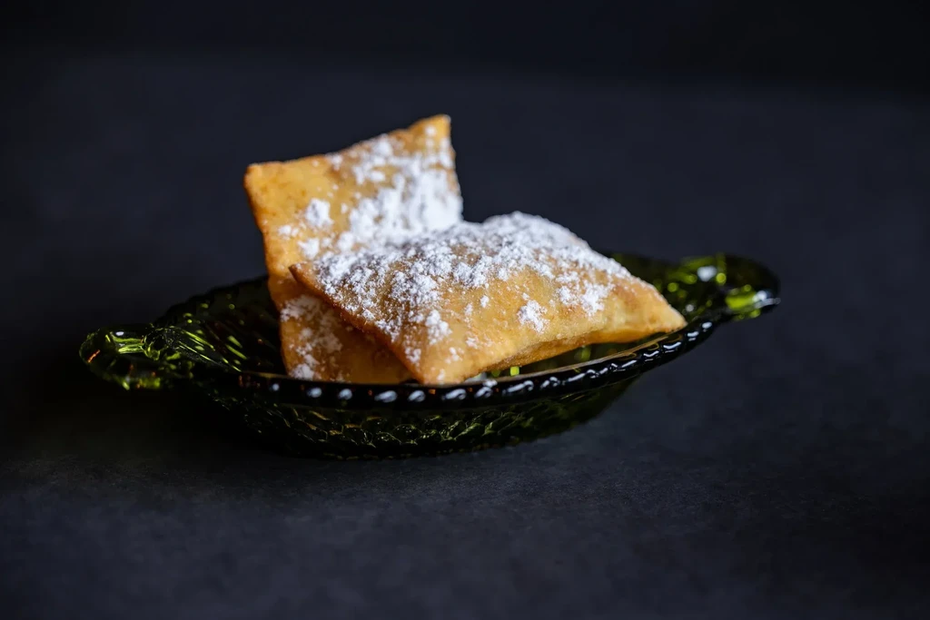 Two golden rectangular fried pastries, sugared, on a scalloped green plate.