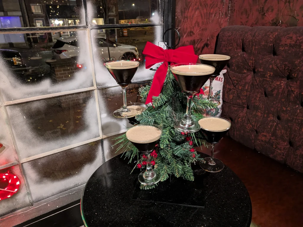 Five martini glasses surrounding a small, decorated Christmas tree on a table.