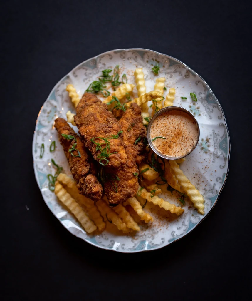 Crispy fried chicken tenders, crinkle-cut fries, and dipping sauce on a plate.
