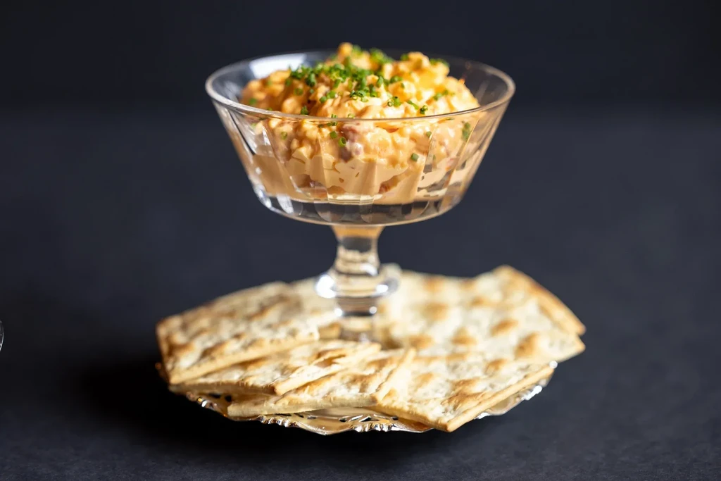 Creamy orange dip with chives in glass bowl, with crackers.