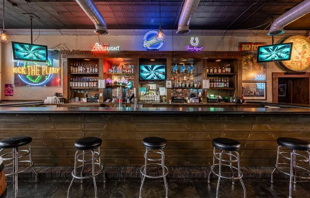 Empty rustic-industrial bar interior with dark wood, brick, and neon signs.