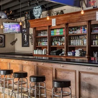 Empty, well-lit modern bar with wooden counter, stocked liquor shelves, brick wall.