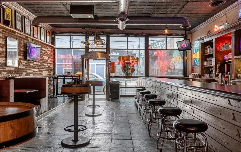 Rustic industrial bar with dark counter, booth seating, brick walls, neon.