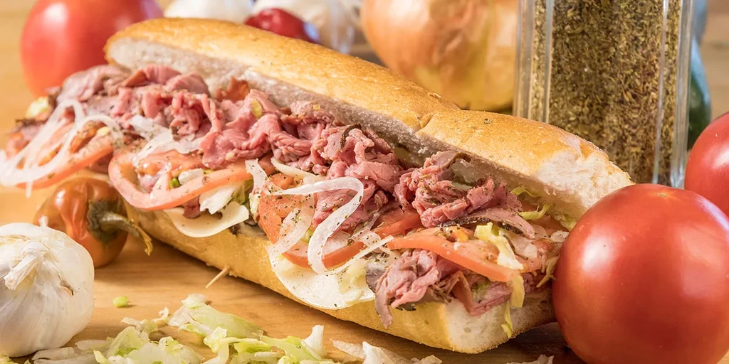 A roast beef sub sandwich on a wooden board with fresh ingredients.
