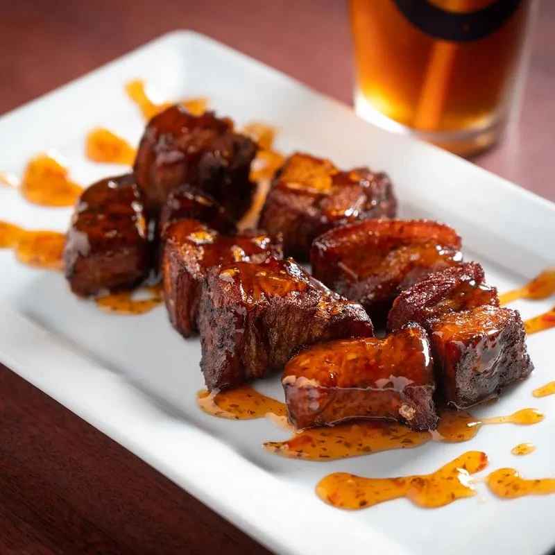 Artfully arranged, richly glazed meat on a white rectangular plate.