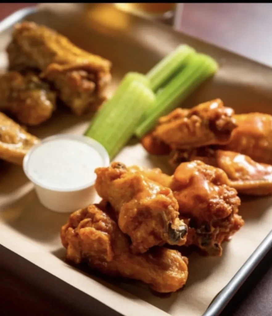 Fried chicken wings, celery sticks, and white dipping sauce on a tray.