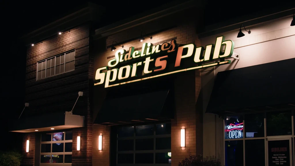 Night view of Sidelines Sports Pub with bright signs and warm lighting.