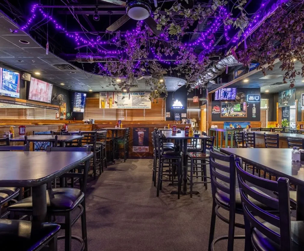 Dimly lit restaurant interior with purple string lights, tables, and TVs.